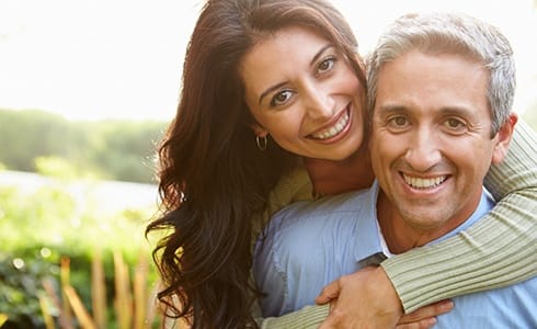 A middle-aged couple hugging and smiling while enjoying the outdoors after seeing their HealthChoice dentist in Oklahoma City