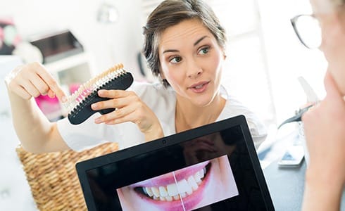 A dentist showing a patient what her smile will look like after receiving veneers and pointing to a shade guide to show her the new color