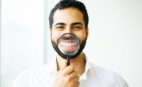 man holding magnifying glass to his smile after dental bonding in Oklahoma City 