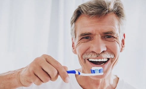 older man brushing his dental bridges in Oklahoma City 