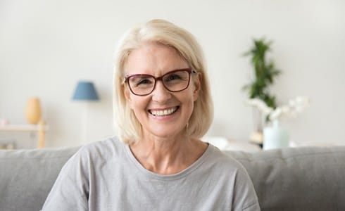 An older woman wearing glasses and a gray shirt, smiling after seeing her Delta Dental dentist in Oklahoma City