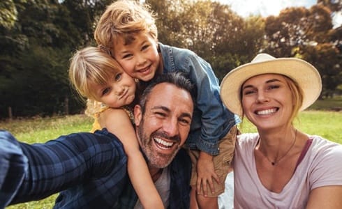 family of four sitting and smiling among the trees