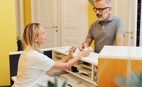 An older man hands his insurance card to a female dental receptionist