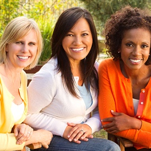 Three middle-aged women all smiling and showing off their dental implants in Oklahoma City