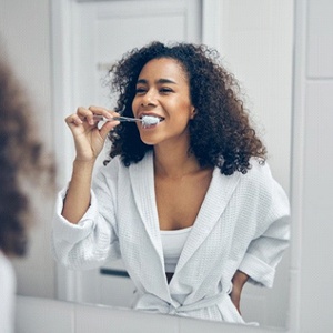 woman in a white bathrobe brushing her teeth