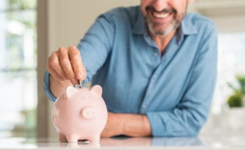 man putting coins into a pink piggy bank 