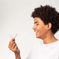 Teenage boy smiling while holding clear aligner