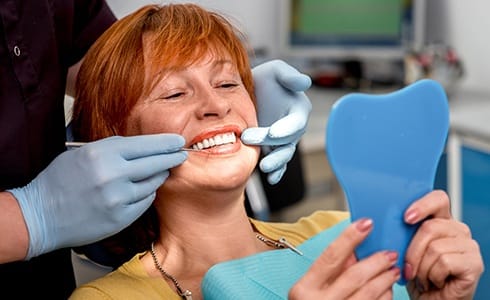 Woman looking at smile in mirror during preventive dentistry appointment