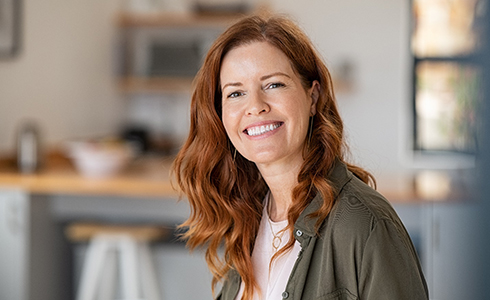Red-haired woman standing in kitchen smiling 