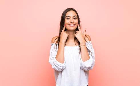 Woman pointing to her smile standing with pink background