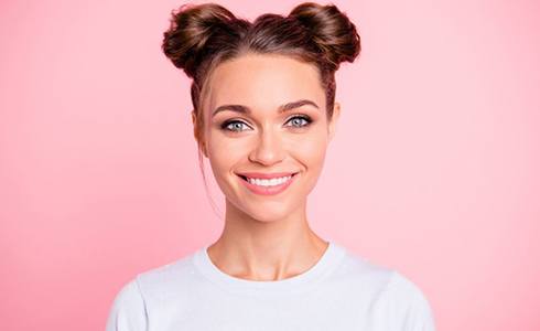 woman with space buns smiling against pink background 
