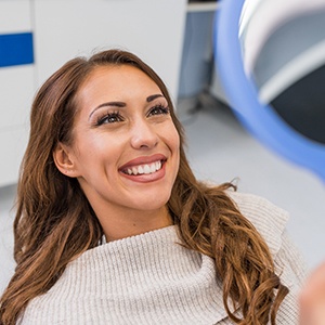 Woman smiling in dental chair while looking into mirror