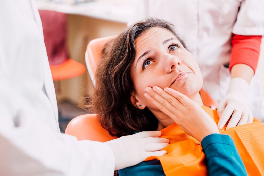 Woman in dental chair with hand to cheek looking at dentist in white coat